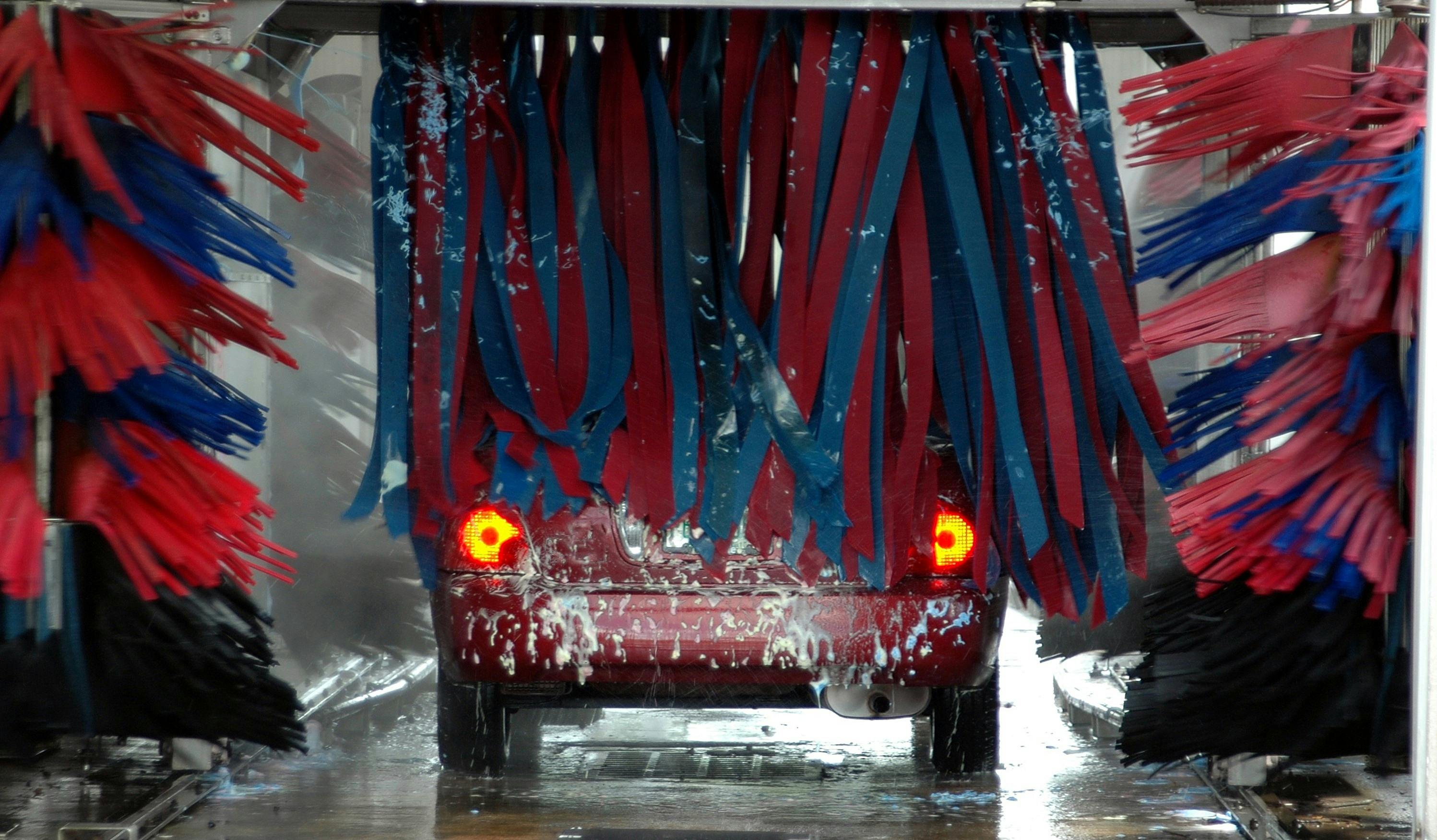 Automatic car wash tunnel with spinning brushes touching vehicle